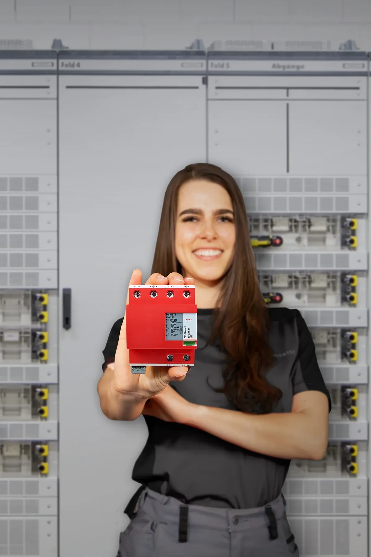 Frau hält rotes elektrisches Gerät vor Schaltschränken.